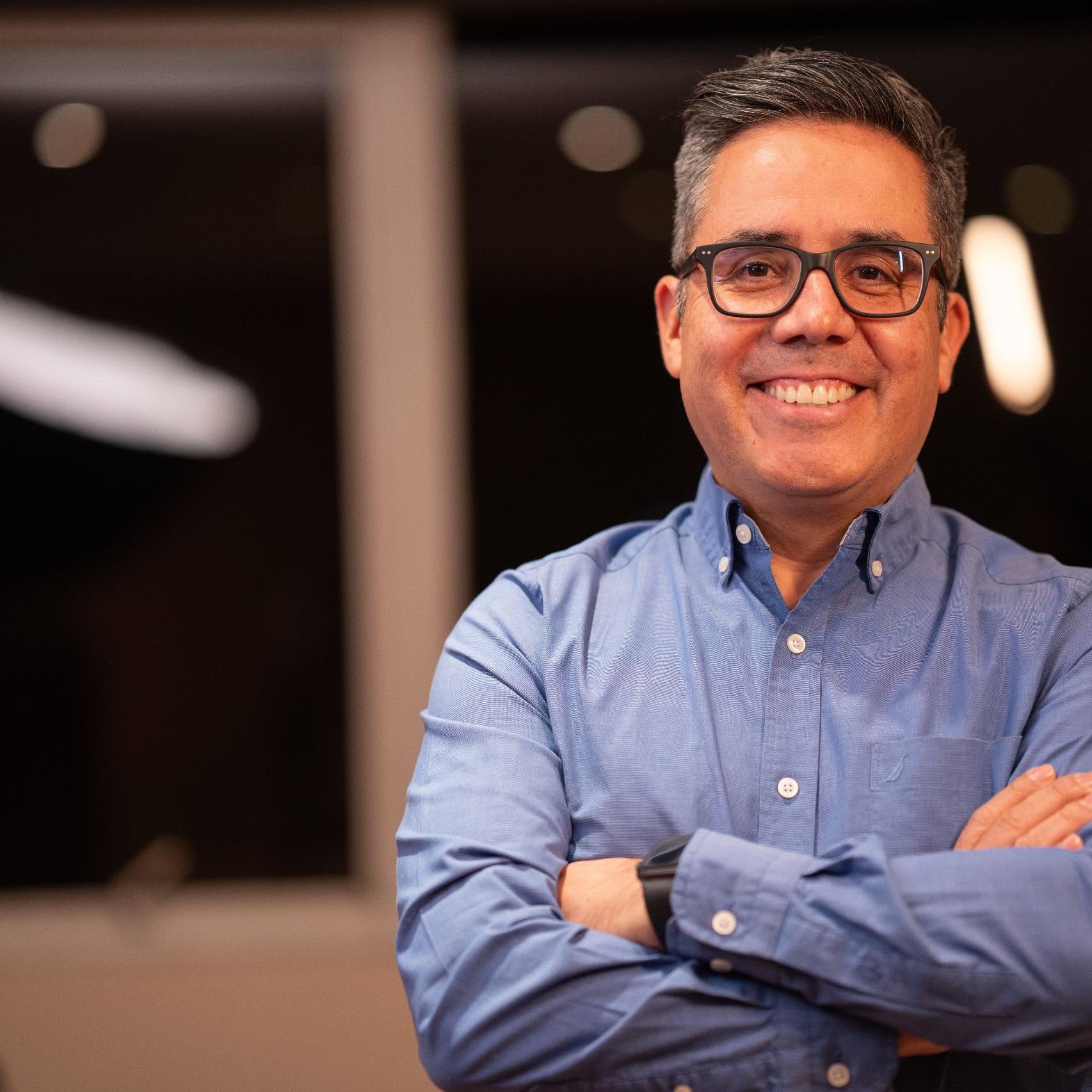 Dr. Salvador Villalpando sonriendo, con camisa azul y lentes
